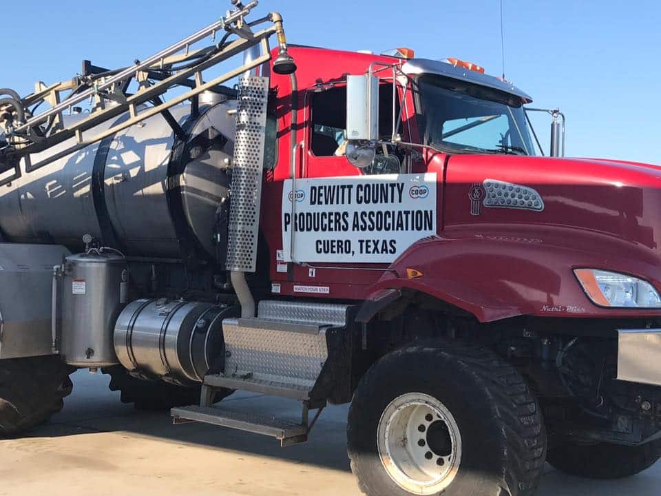 A red tanker truck with the inscription 'DEWITT COUNTY PRODUCERS ASSOCIATION CUERO, TEXAS' on its side.