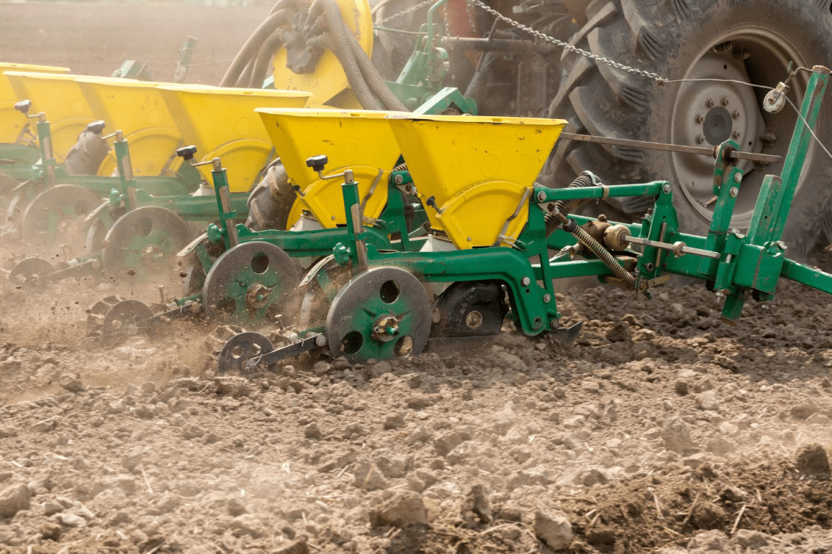 Close-up view of seed planters attached to a tractor, sowing seeds in a dry field.