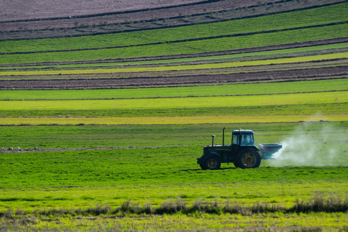 A tractor spraying fertilizer on a large, green agricultural field.