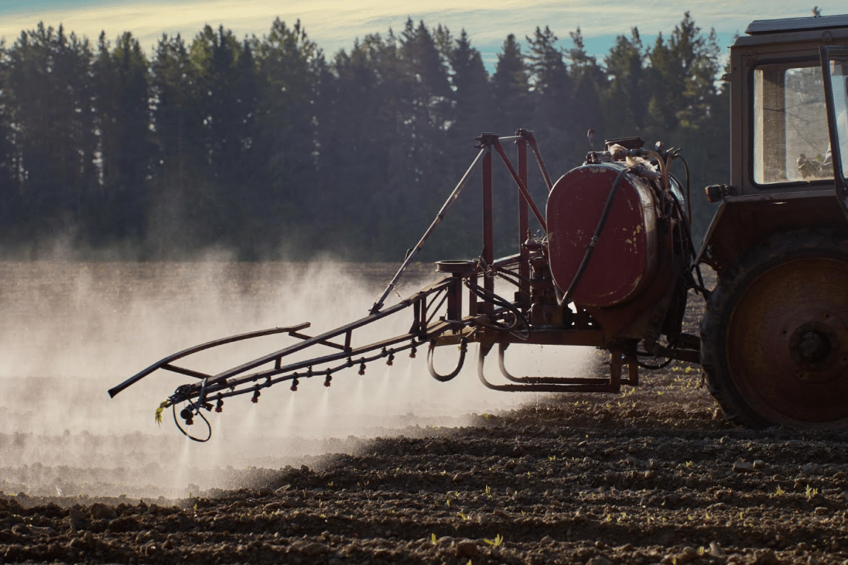 A tractor spraying a field with mist under the early morning light with trees in the background.