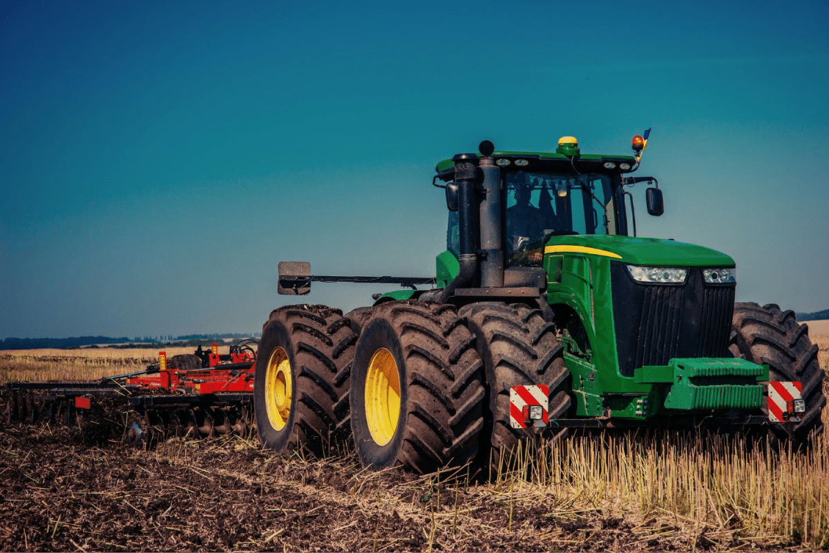 A large green tractor with multiple tires working in a field under a clear blue sky.