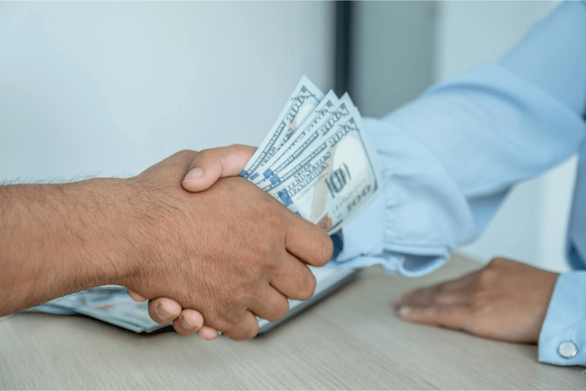 Close-up of two people shaking hands, with one person holding cash in the other hand.