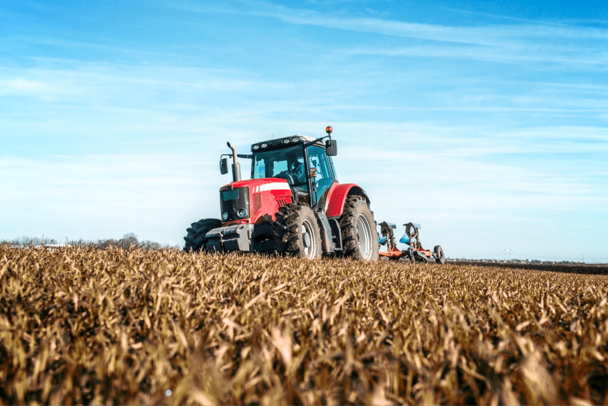 A red tractor plowing a field on a clear day with blue skies.