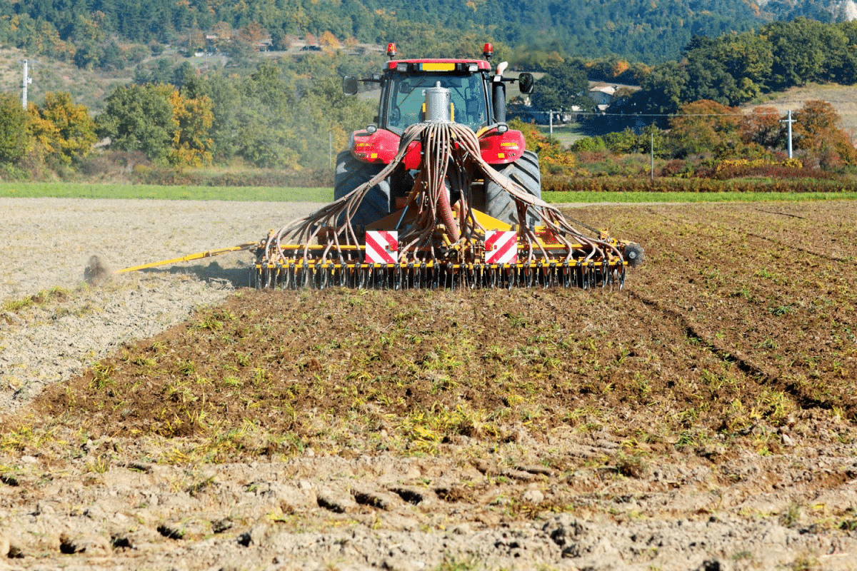 A red tractor with a seeding machine planting seeds in a freshly plowed field.